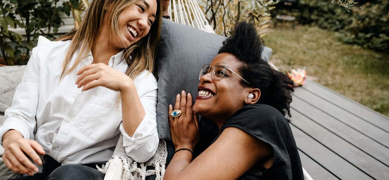 Deux femmes face &agrave; face en train de rire et de discuter. La femme de droite a un Buds2 Pro dans son oreille gauche.