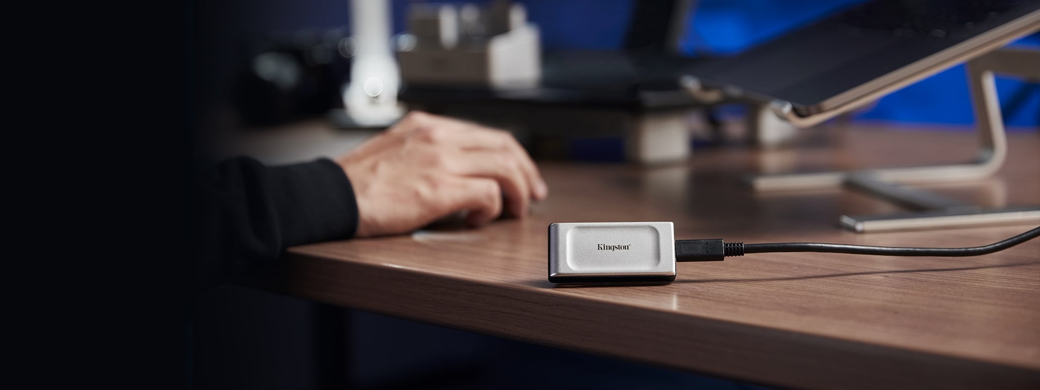 Un SSD externe XS2000 est pos&eacute; sur le bord d&rsquo;un bureau &agrave; c&ocirc;t&eacute; d&rsquo;un ordinateur portable sur un support