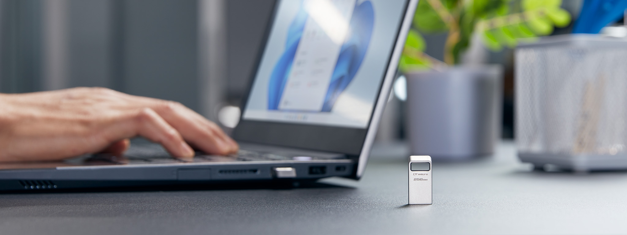 Une cl&eacute; USB DT Micro debout sur un bureau, avec une personne travaillant sur un ordinateur portable en arri&egrave;re-plan