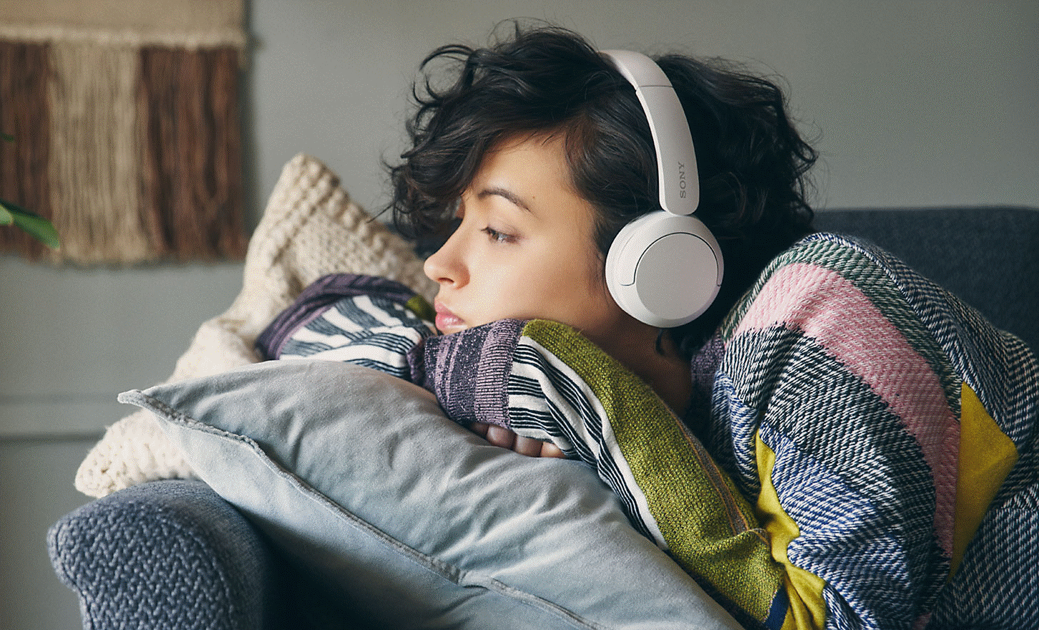 Image d'une femme allongée sur un canapé gris portant un casque Sony WH-CH520 blanc