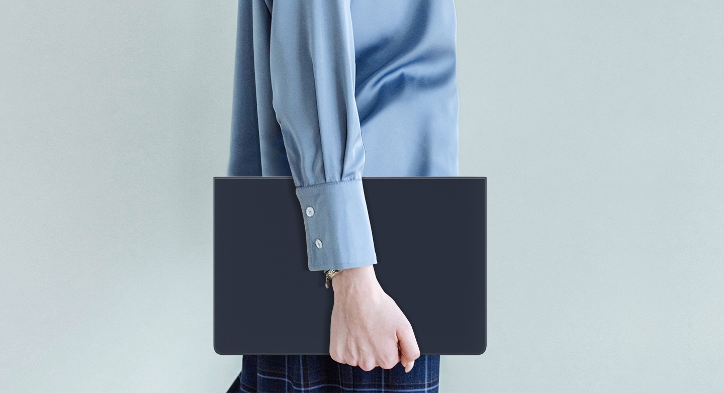 Une personne portant une chemise bleue marche en tenant une Galaxy Tab S9 &eacute;quip&eacute;e d&rsquo;un Book Cover Keyboard fin.