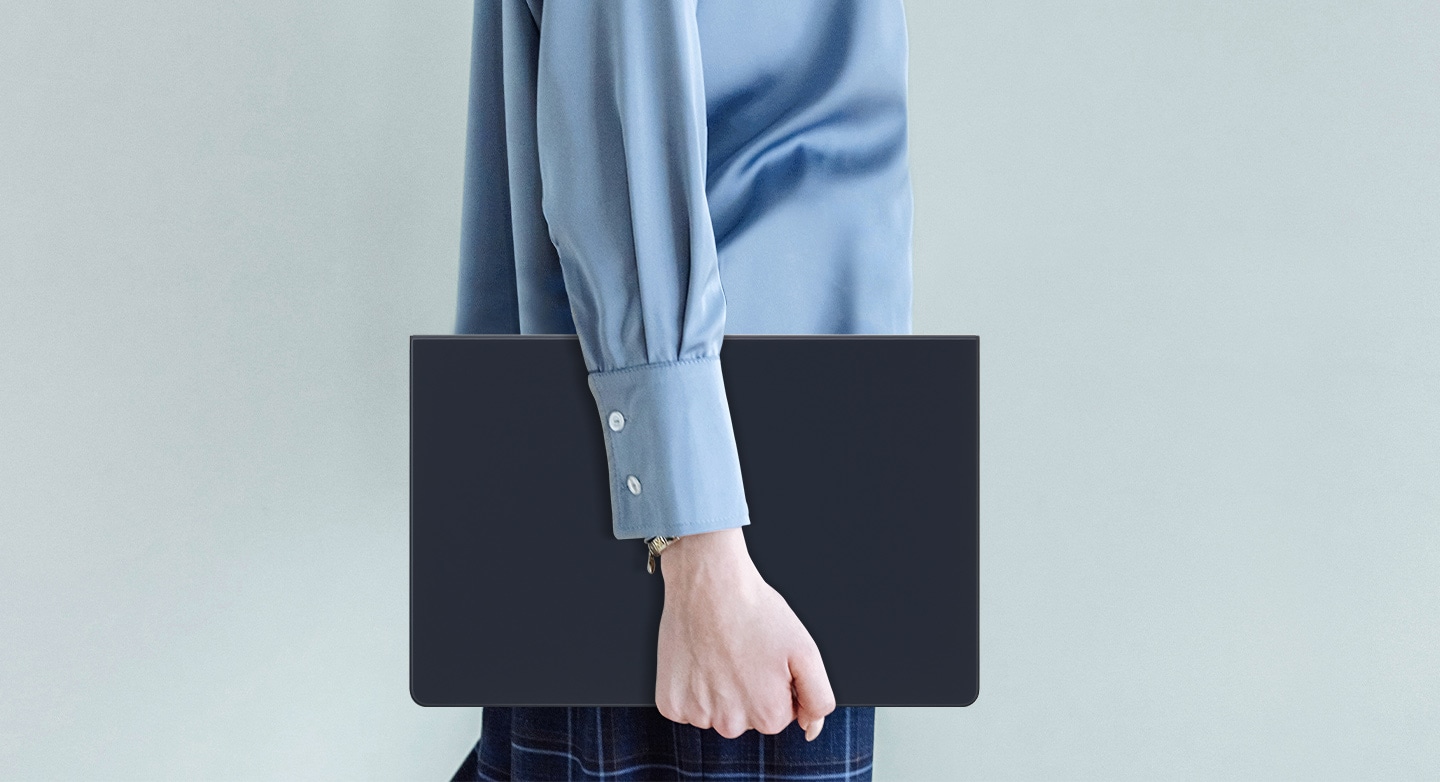 Une personne v&ecirc;tue d&rsquo;une chemise bleue est pr&eacute;sent&eacute;e en train de marcher tout en tenant une Galaxy Tab S9+ prot&eacute;g&eacute;e par un Book Cover Keyboard Slim.