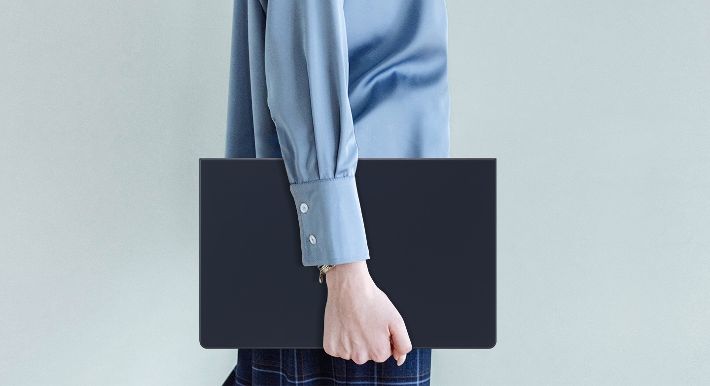 Une personne portant une chemise bleue marche en tenant une Galaxy Tab S9 Ultra &eacute;quip&eacute;e d&rsquo;un Book Cover Keyboard fin.