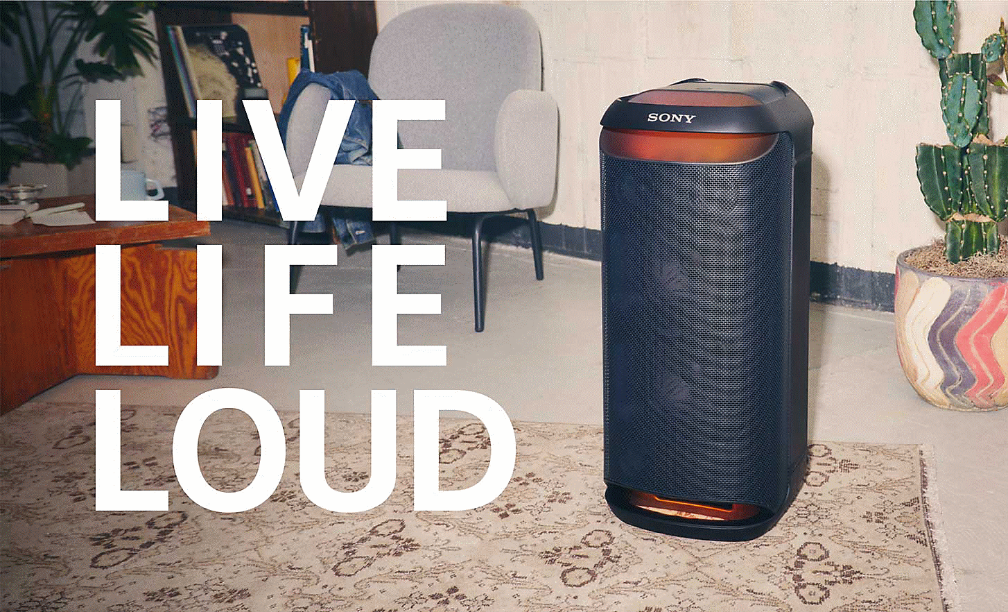 Image de l'enceinte SRS-XV800 pos&eacute;e sur un tapis dans une pi&egrave;ce pourvue d'un fauteuil et d'un cactus, avec les mots LIVE LIFE LOUD