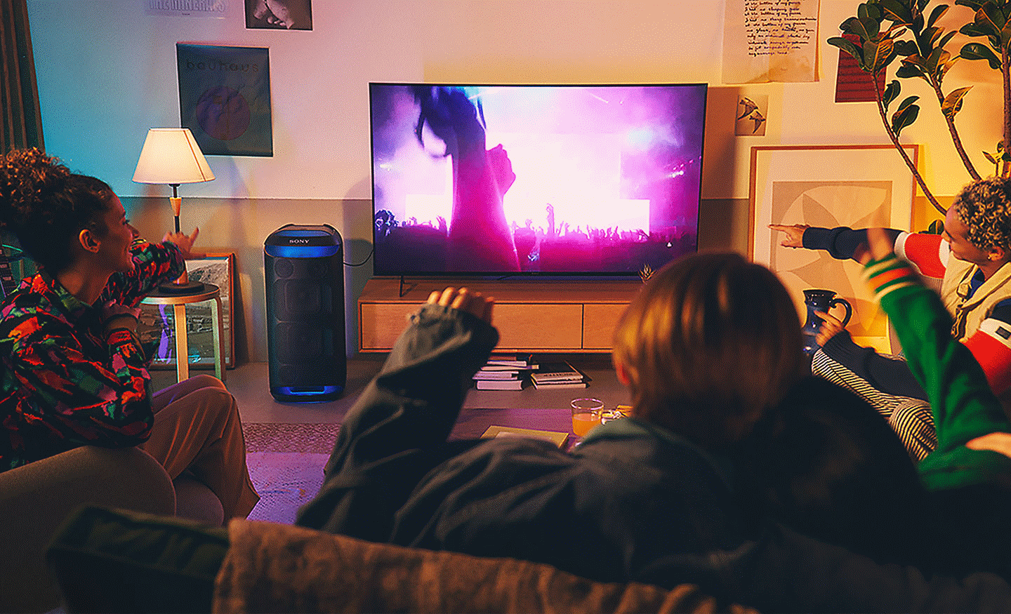Image de personnes dans un salon regardant un concert sur un t&eacute;l&eacute;viseur plac&eacute; &agrave; c&ocirc;t&eacute; d'une enceinte SRS-XV800 avec un &eacute;clairage d'ambiance bleu