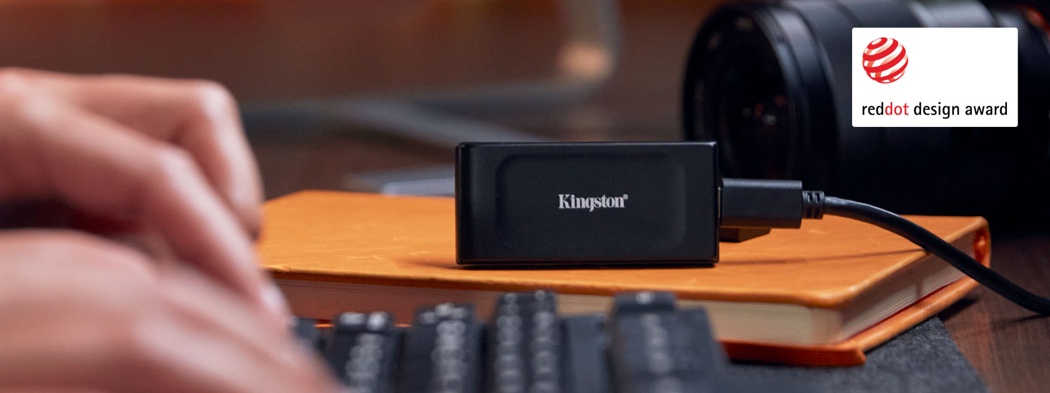 Un SSD externe XS1000 est posé sur un livre, avec des mains sur un clavier au premier plan