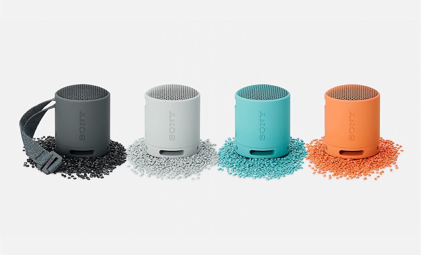 Image des enceintes SRS-XB100 en noir, blanc, bleu et orange reposant sur des granul&eacute;s de plastique de couleur assortie