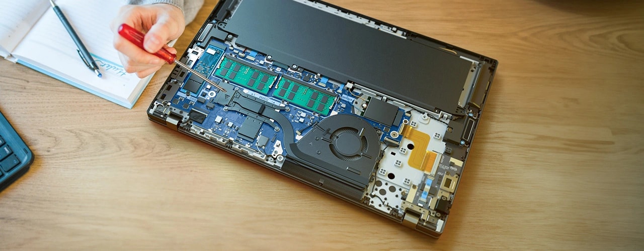 Lenovo ThinkPad T16 Gen 3 (16'' Intel) laptop — on a desk, cover removed to show internal components, with a hand pointing a screwdriver