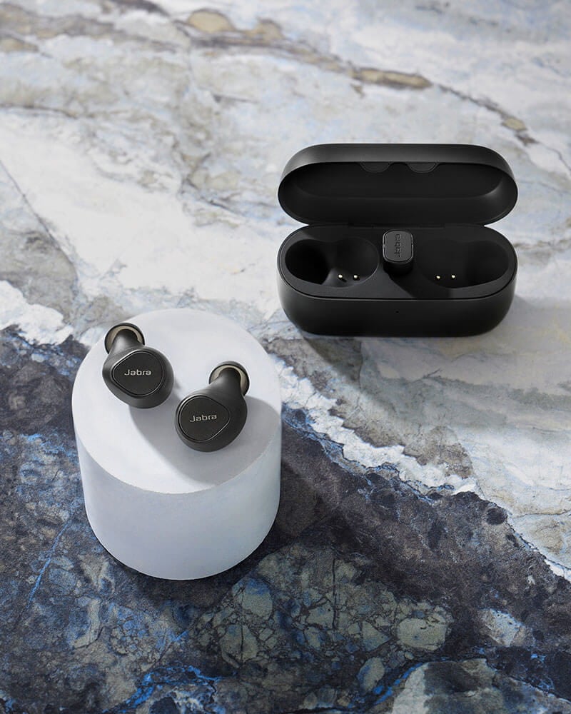 Black Elite 5 earbuds and case in front of a dice game on a bar table