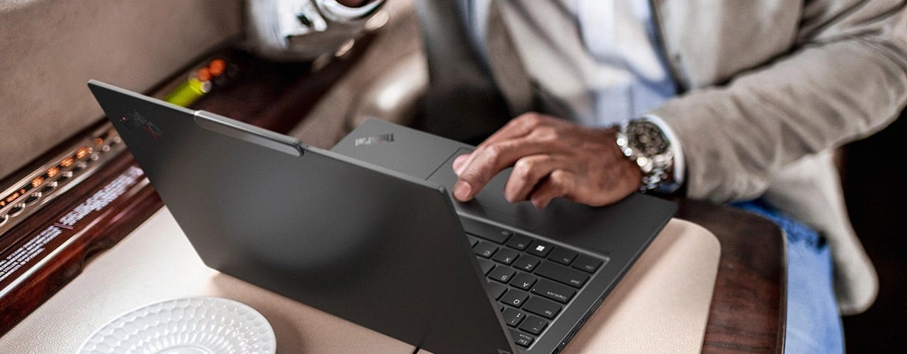 Vue de dessus d’une personne dans un train en train d’utiliser le PC portable Lenovo ThinkPad X1 Carbon Gen 12 sur une table.