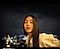 Photo d&rsquo;une femme en plein air la nuit avec un visage &eacute;clair&eacute; et des lumi&egrave;res de ville floues en arri&egrave;re-plan. Le texte indique Photo prise avec le Galaxy S24 FE #withGalaxy.