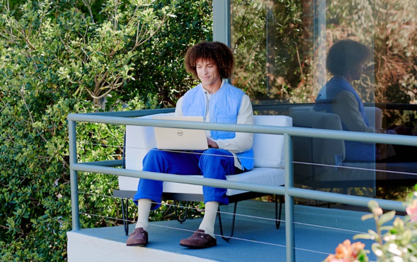 Un homme est assis sur son balcon et se concentre sur son ordinateur portable.