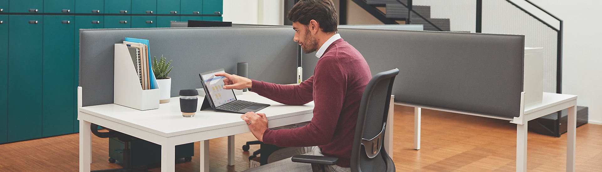 Person seated at a cubicle desk in an office using a Microsoft Surface