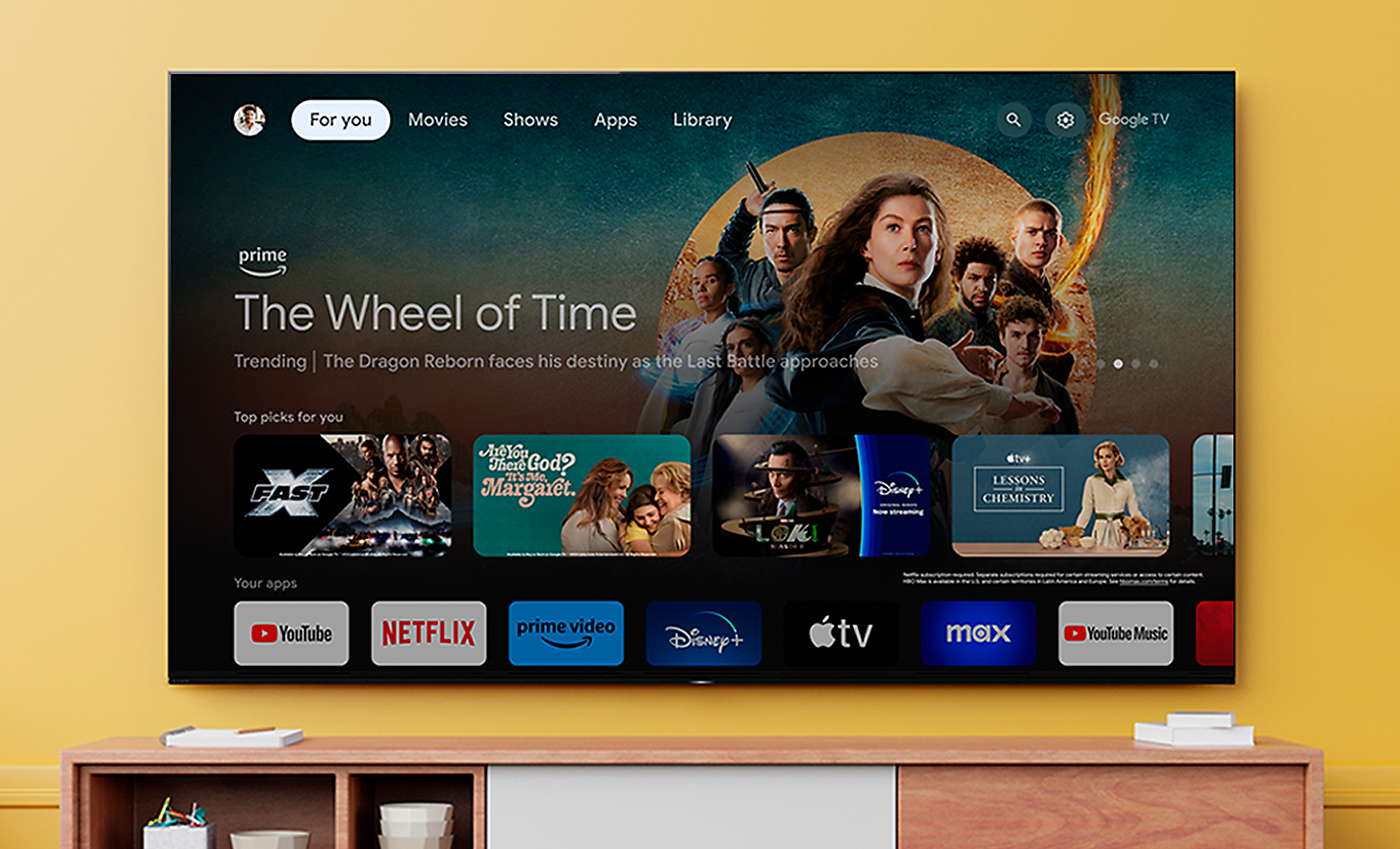 Télévision fixée au mur au-dessus d'un meuble en bois avec une capture d'écran de la série télévisée « La Roue du temps » avec diverses applications mises en évidence en dessous
