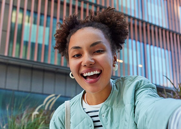 A selfie of a smiling woman with a modern building in the background.