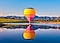 A colorful hot air balloon floating above a lake, with its reflection on the water.