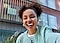 A selfie of a smiling woman with a modern building in the background.