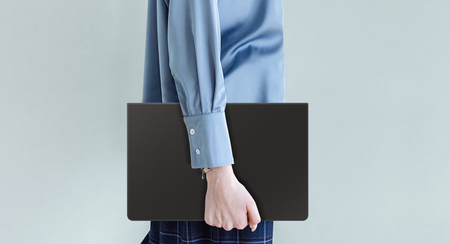 Une personne portant une chemise bleue est vue en train de marcher tout en tenant une Galaxy Tab S10 FE+ recouverte d'un Book Cover Keyboard Slim.