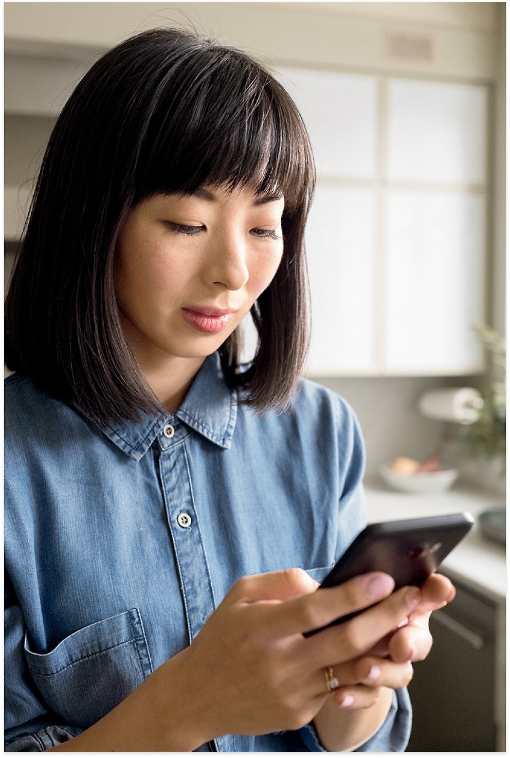 Femme portant un haut de couleur bleue consultant son t&eacute;l&eacute;phone avec ses deux mains