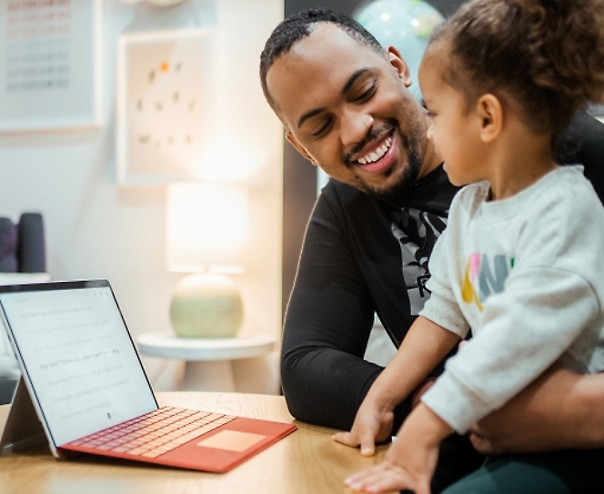 Personne souriant et regardant un enfant, avec un ordinateur portable pos&eacute; sur la table