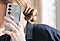 Une femme tient un Galaxy S25+ &eacute;quip&eacute; de la Standing Grip Case en Gris. Un doigt tenant le t&eacute;l&eacute;phone est plac&eacute; sous la poign&eacute;e r&eacute;glable.