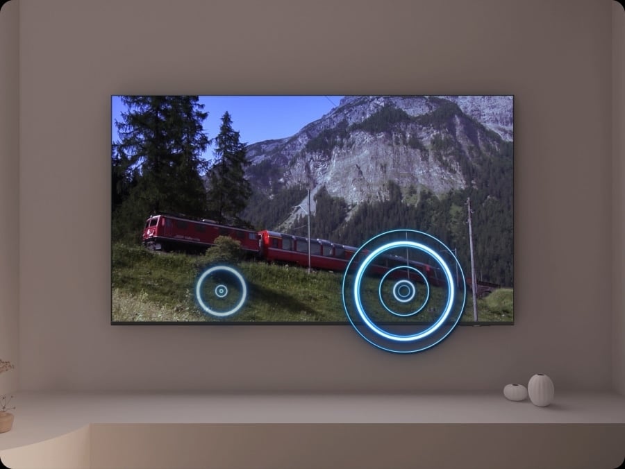 A TV depicts a scene of a train passing by a scenic outdoor location. As it does, sound waves appear near where the train touches the tracks, indicating the noise within the scene.