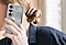 Une femme tient un Galaxy S25 &eacute;quip&eacute; de la Standing Grip Case en Gris. Un doigt tenant le t&eacute;l&eacute;phone est rang&eacute; sous la poign&eacute;e r&eacute;glable.