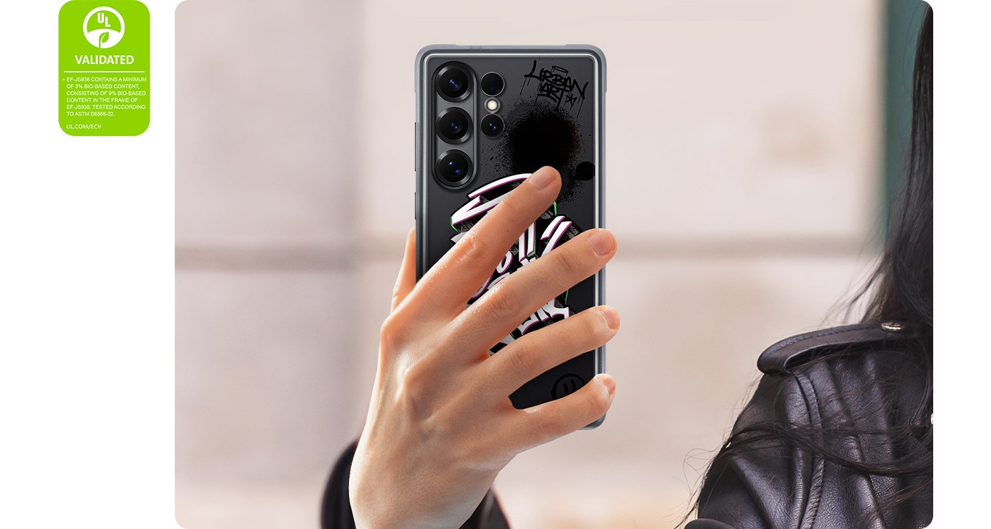 Une personne tient un Galaxy S25 Ultra &eacute;quip&eacute; de la Rugged Case. Le t&eacute;l&eacute;phone est vu de dos, les mains le long des motifs de la coque. &Agrave; gauche, une Certification de d&eacute;claration environnementale UL indique&nbsp;: &laquo;&nbsp;EF-JS938 CONTIENT UN MINIMUM DE 3% DE CONTENU &Agrave; BASE BIOLOGIQUE, COMPRENANT 9% DE CONTENU &Agrave; BASE BIOLOGIQUE DANS LE CADRE DE EF-JS938, TEST&Eacute; SELON ASTM D6866-22. UL.COM/ECV&nbsp;&raquo;.