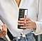 Une jeune femme en tenue semi-formelle marche &agrave; l&rsquo;ext&eacute;rieur, tenant un&nbsp;Galaxy Z Fold5&nbsp;recouvert d&rsquo;une coque verticale avec sangle, les doigts gliss&eacute;s sous une sangle rouge. Des accessoires color&eacute;s sont fix&eacute;s &agrave; la partie inf&eacute;rieure de l&rsquo;&eacute;tui.