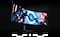A curved monitor shows two characters in astronaut suits going towards a neon blue circle in a dark city.