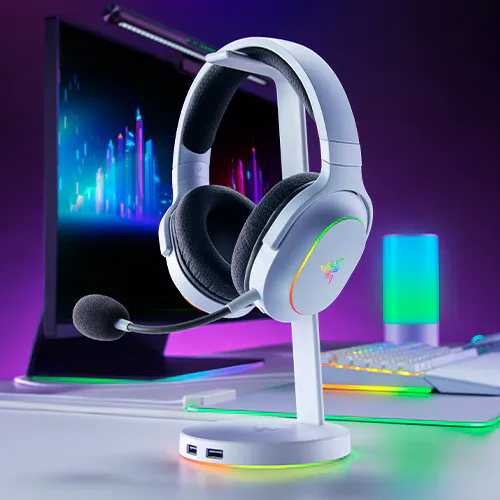 Wireless gaming headset with a built-in microphone on a stand, in front of a colorful computer monitor, &Eacute;CLAIRAGE RGB on desk and equipment.