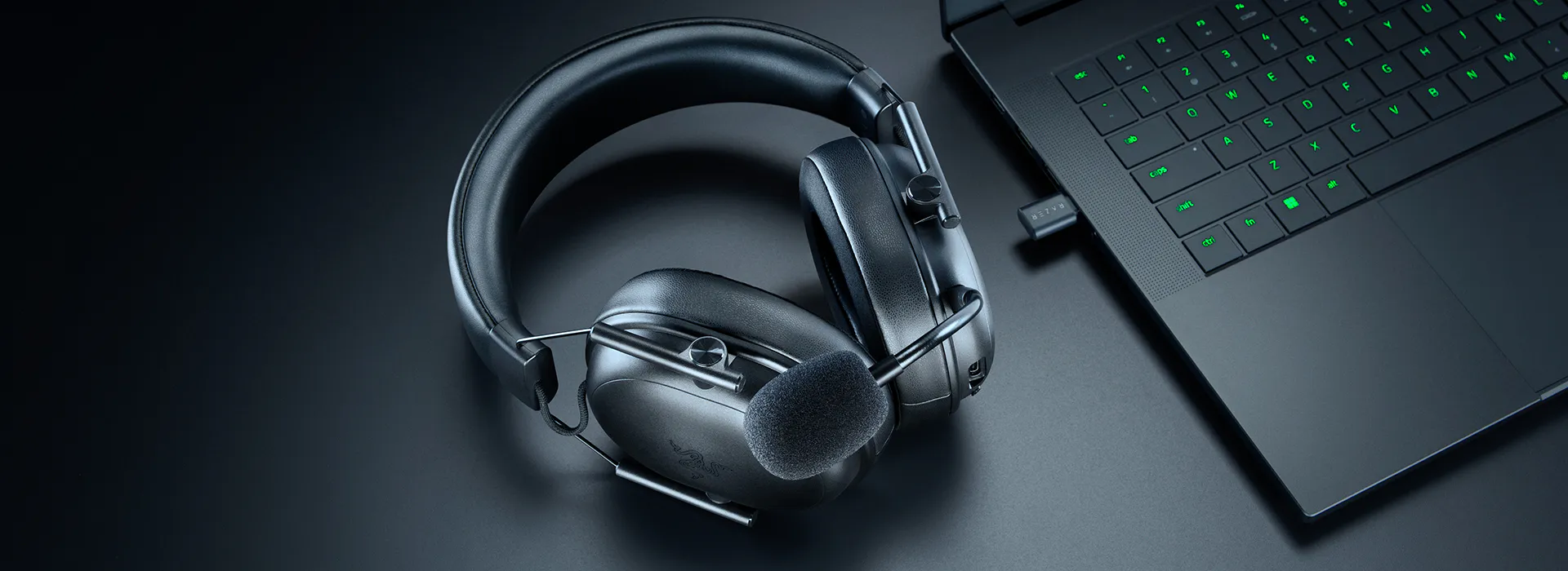 Casque sans fil avec microphone et ordinateur portable noir avec clavier r&eacute;tro&eacute;clair&eacute; en vert sur une surface sombre.