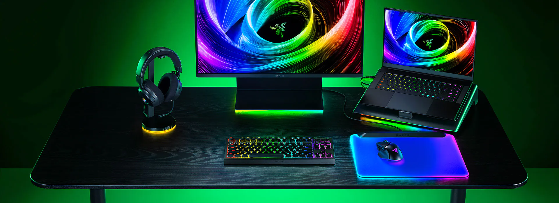 Une configuration de jeu avec un grand moniteur Razer, un clavier m&eacute;canique RVB, une souris RVB sur un tapis de souris, un ordinateur portable avec un &eacute;cran color&eacute; et des &eacute;couteurs noirs.