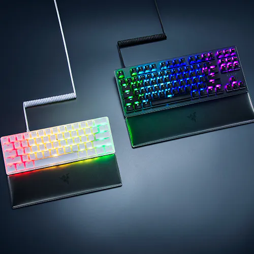 Deux claviers de jeu &eacute;clair&eacute;s avec touches r&eacute;tro&eacute;clair&eacute;es RVB, l'un avec un cadre blanc et l'autre avec un cadre noir, sur une surface sombre.