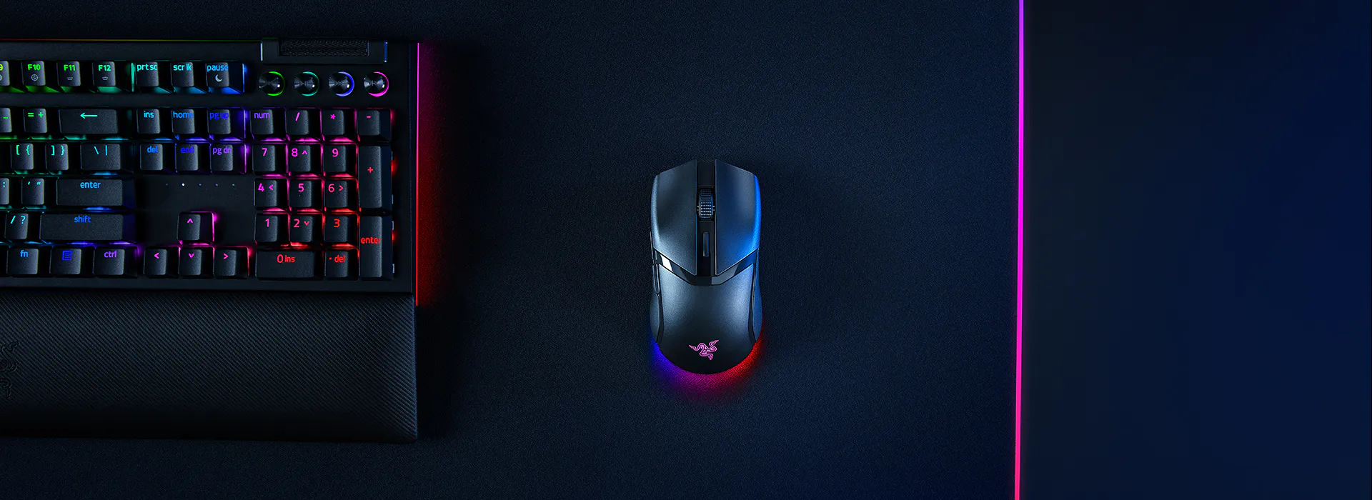 Une configuration de jeu avec un clavier m&eacute;canique noir avec r&eacute;tro&eacute;clairage RVB, une souris filaire avec &eacute;clairage RVB, sur un tapis de jeu sombre avec des reflets LED roses.