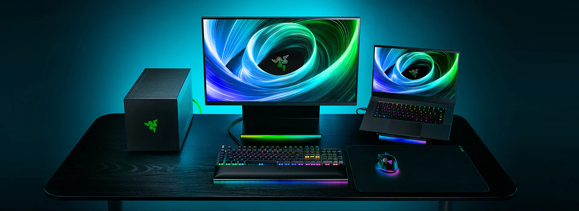 A gaming setup with a Razer desktop, a mounted monitor, a laptop with RGB keyboard, mouse, and mouse pad, all with RGB lighting.