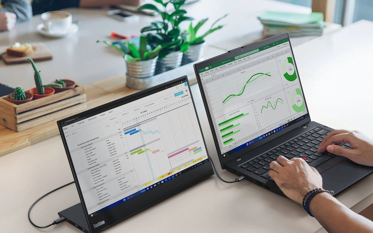 Ordinateur portable Lenovo ThinkPad L14 Gen 6 (Intel 14 pouces) sur un bureau, connecté à un moniteur ThinkVision tandis que deux mains tapent sur le clavier : aperçu avant gauche, capot ouvert, avec plusieurs graphiques à l'écran