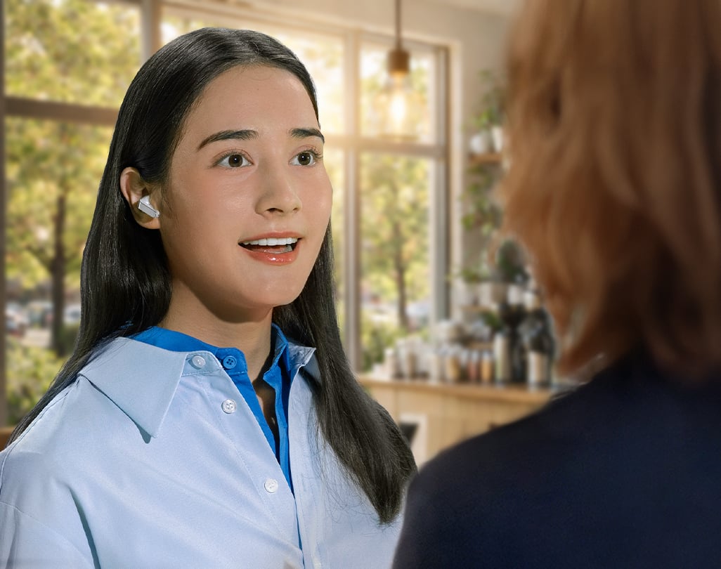 Une femme utilisant un Galaxy Buds4 Pro blanc en conversation avec une autre personne, illustrant la fonction Voice Detect.