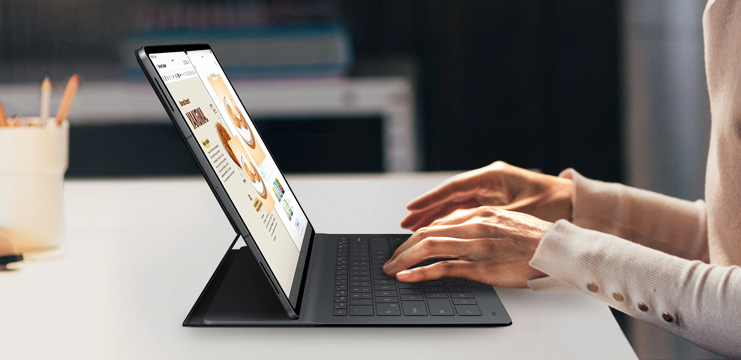 Une personne tape sur la Galaxy Tab S11 Ultra en utilisant le Book Cover Keyboard Slim. L'écran affiche Drawing Assist et Samsung Notes ouverts côte à côte. Le design élégant du clavier complète celui de la tablette, mettant en valeur une configuration professionnelle soignée pour un travail multitâche créatif.