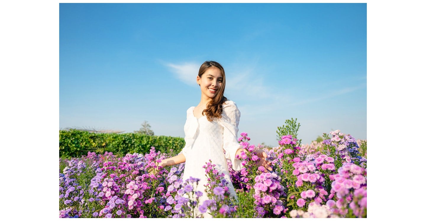 Une femme en robe blanche, debout à l’extérieur au milieu d’une multitude de fleurs, posant pour une photo.