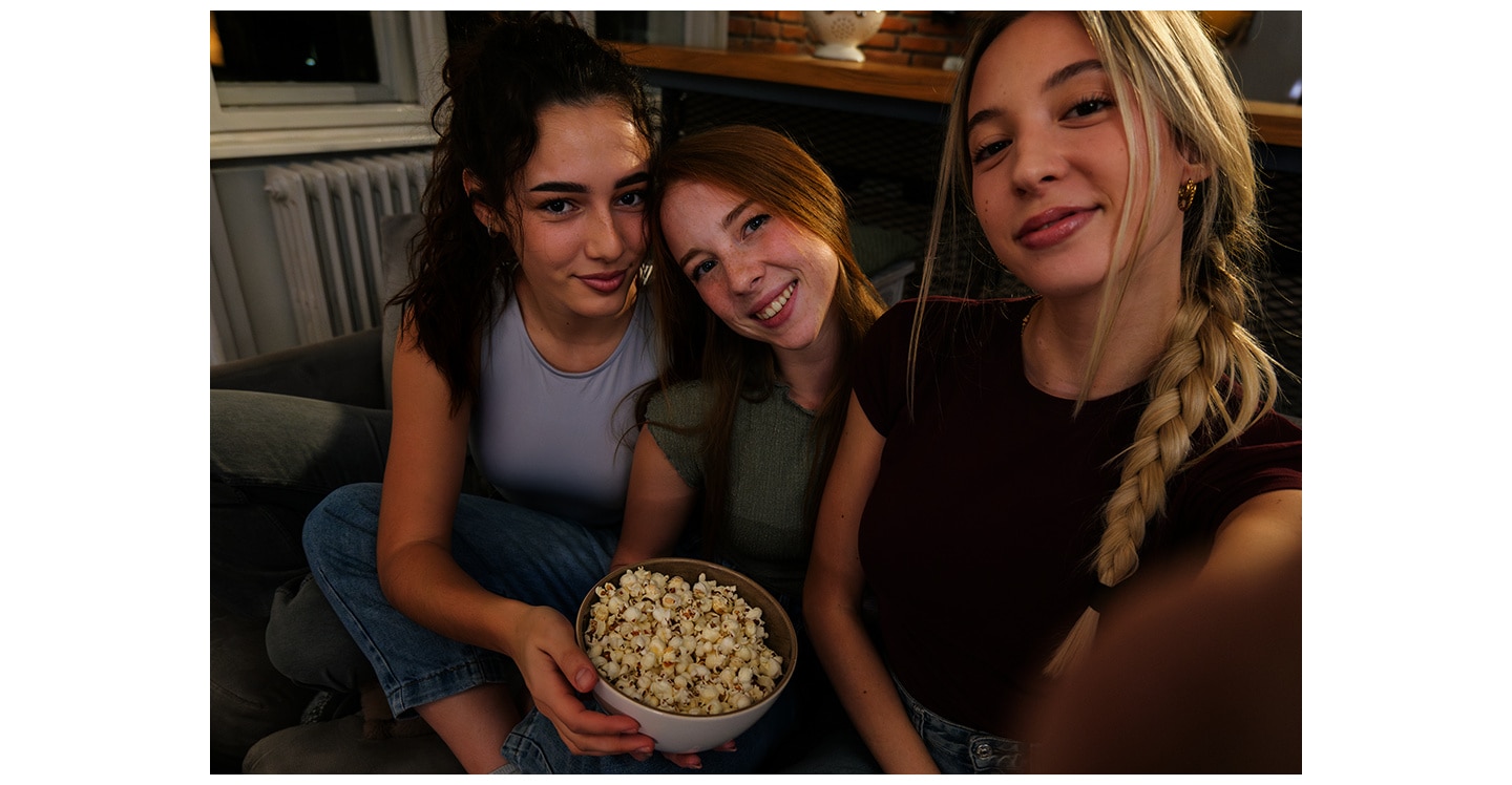 Trois filles assises sur un canapé, dans une pièce faiblement éclairée, en train de se prendre en photo. L’une d’elles prend la photo avec un Galaxy&nbsp;A37 5G équipé de la fonction Nightography, qui permet d’obtenir des clichés lumineux aux détails éclatants.
