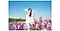 Une femme en robe blanche, debout à l’extérieur au milieu d’une multitude de fleurs, posant pour une photo.