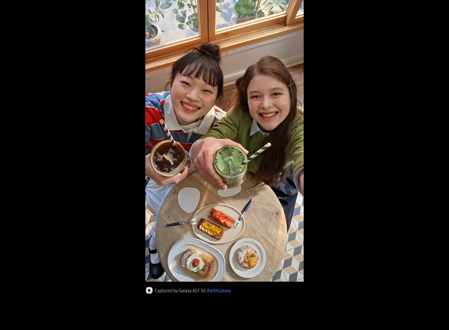 Vidéo selfie de deux jeunes femmes en train de prendre un brunch dans un café lumineux, prise en plongée avec l’appareil photo frontal du Galaxy A57 5G. Les détails de la vidéo sont vifs et colorés grâce à la fonctionnalité Super HDR. En bas apparaît une icône d’appareil photo avec le texte «&nbsp;Capturée par Galaxy A57 5G&nbsp;» et le hashtag Galaxy.