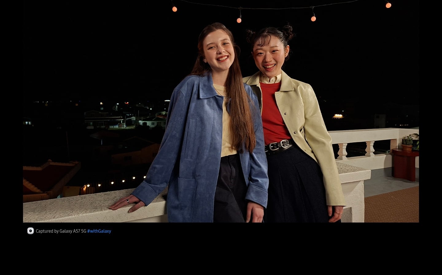 Vidéo de deux jeunes femmes qui sourient et agitent les mains tout en s’appuyant sur une terrasse extérieure la nuit, capturée à l’aide du système d’appareil photo du Galaxy A57 5G. Les détails de la vidéo sont clairs et lumineux grâce à la fonctionnalité Nightography optimisée. En bas apparaît une icône d’appareil photo avec le texte «&nbsp;Capturée par Galaxy A57 5G&nbsp;» et le hashtag Galaxy.