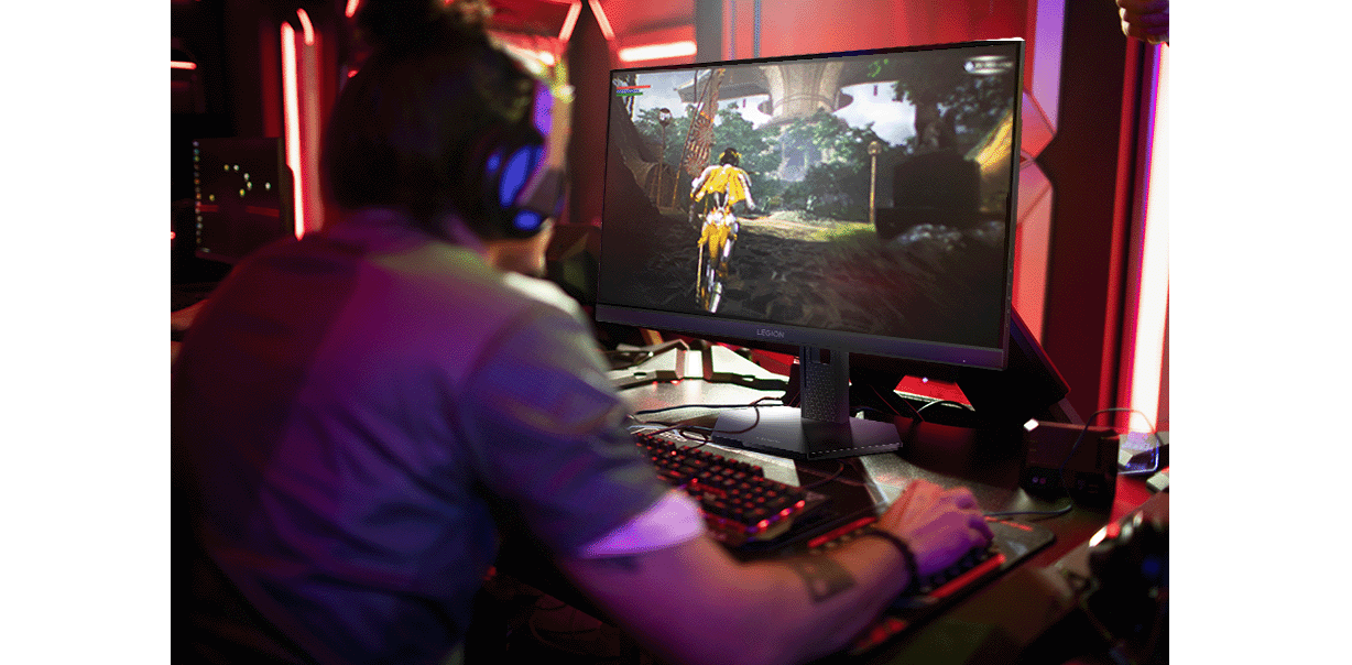 Une personne portant des écouteurs joue sur un moniteur Lenovo Legion-27q-11 dans une pièce avec un éclairage rouge et violet.