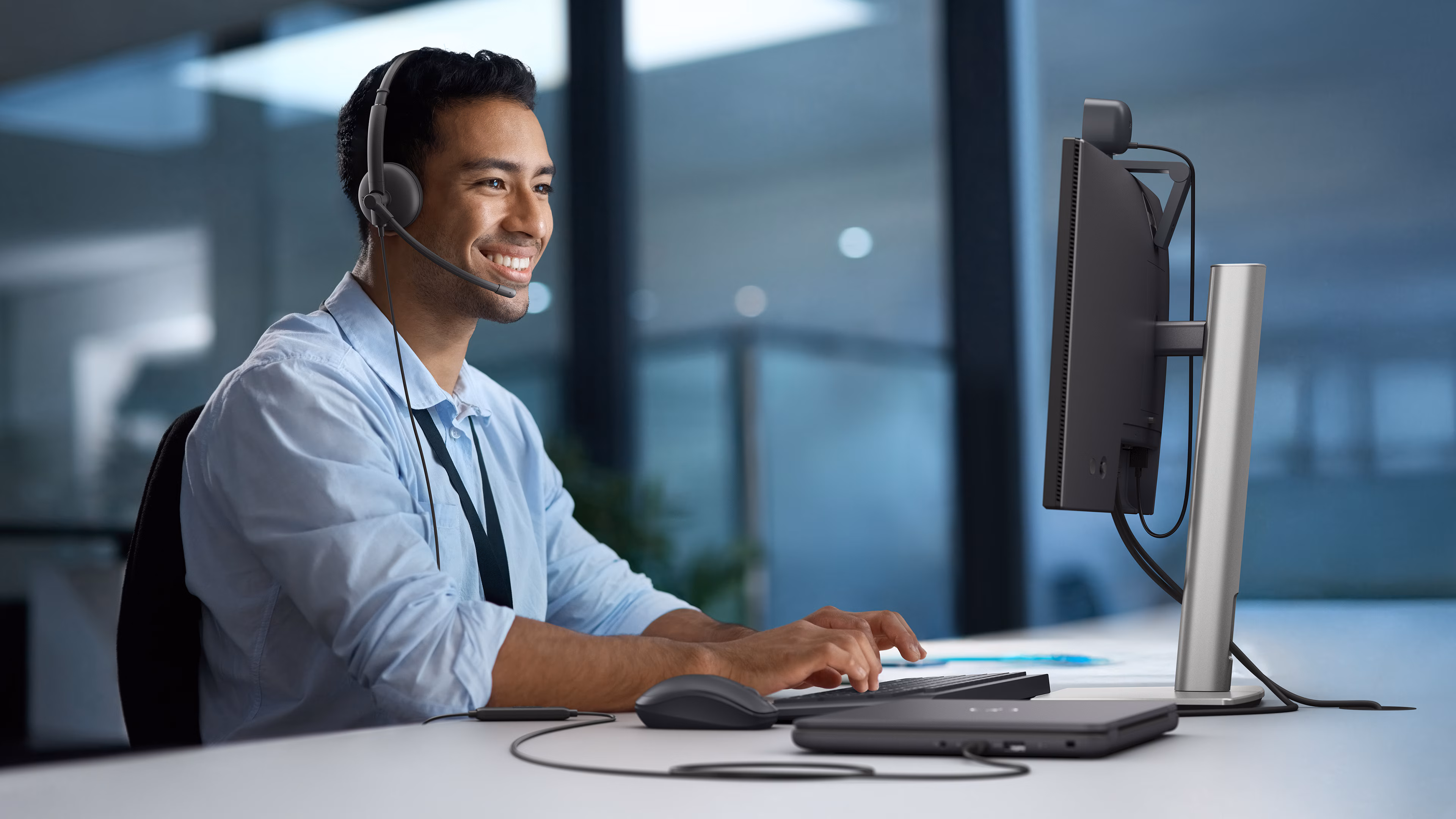 Personne travaillant dans un bureau et portant un casque filaire Dell tout en utilisant un écran, un ordinateur portable, un clavier et une souris Dell.