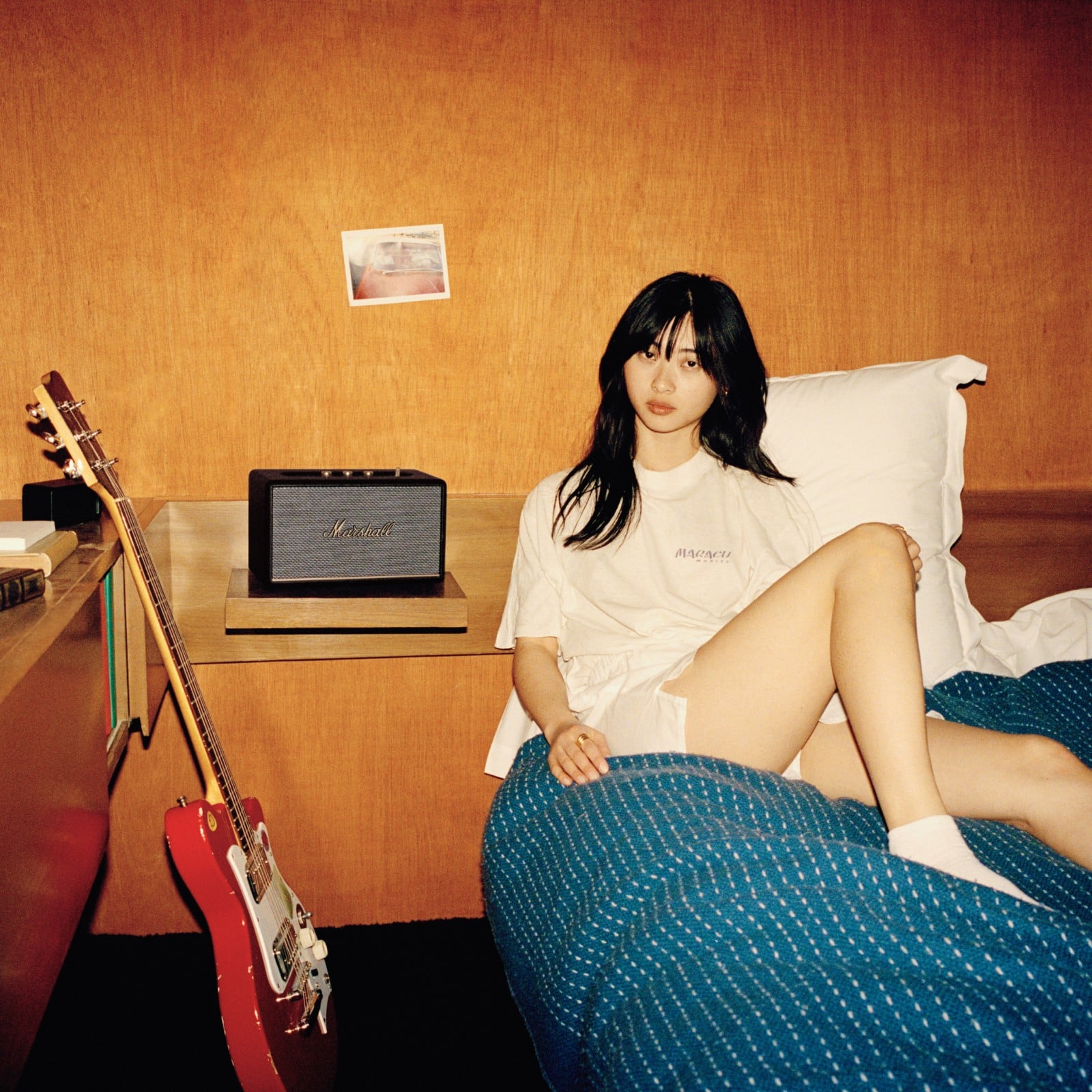 Une fille assise sur un lit à côté d'une guitare Marshall ACTON III BLACK.