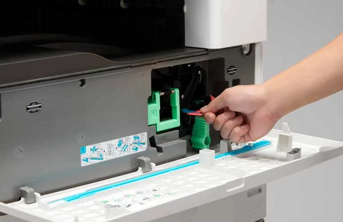 يد تسحب لسانًا داخل الغطاء الأمامي المفتوح لطابعة Ricoh IM 2702، والوحدات الداخلية في المتناول من الأمام