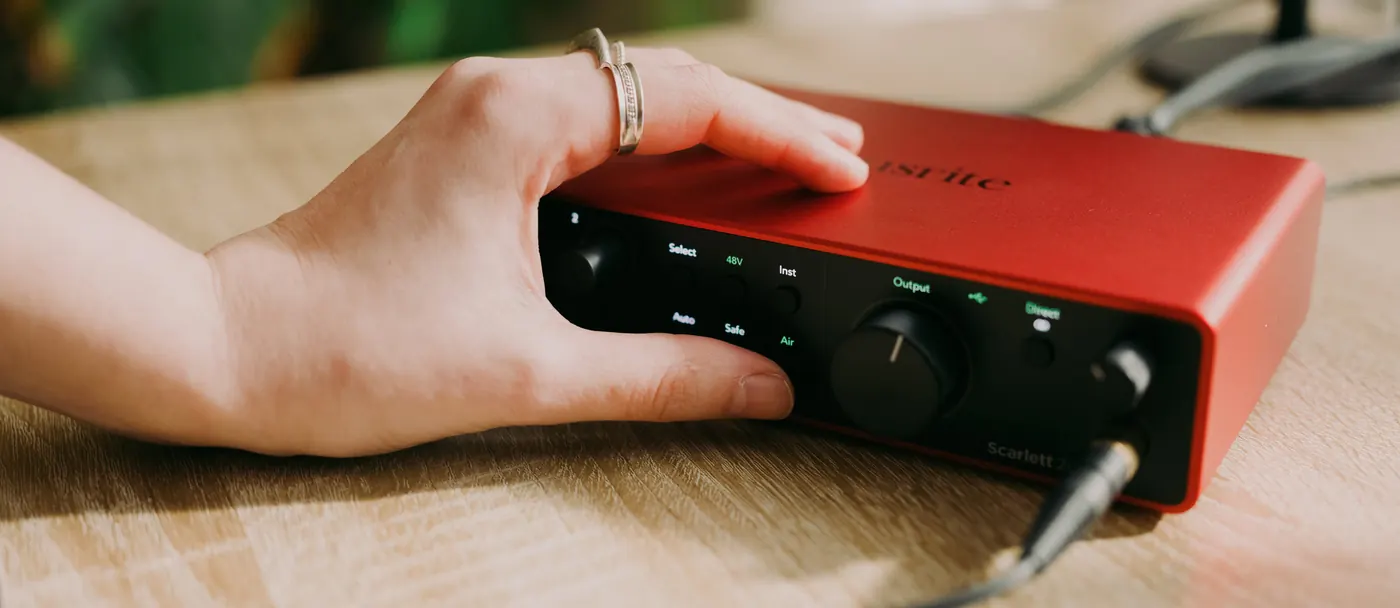 Main posée sur l'interface Scarlett 2i2 installée sur un bureau en bois, câble branché dans la prise casque