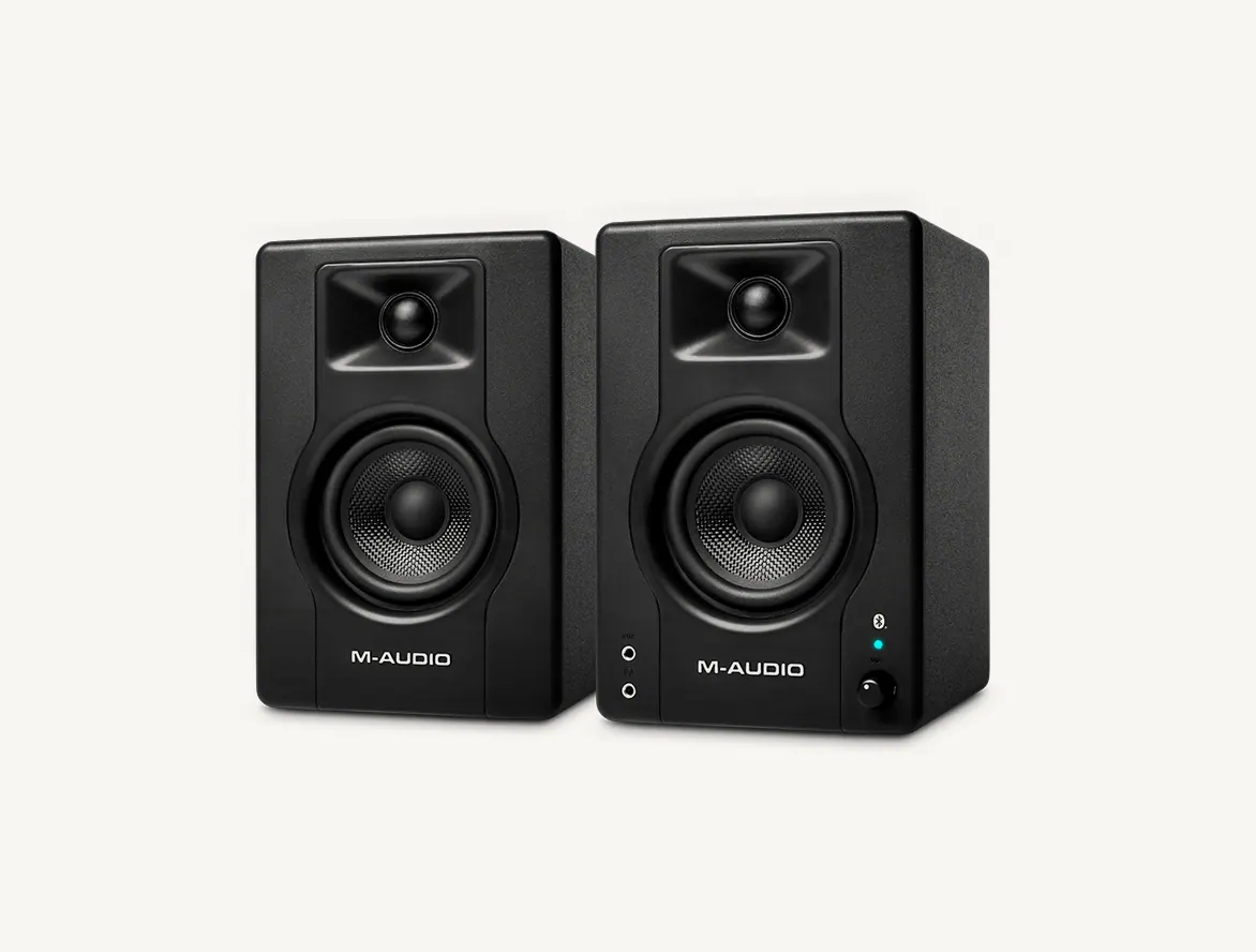 Paire d'enceintes M-Audio BX3 BT vue de trois quarts : façades noires, boomers Kevlar et tweeters, voyant et bouton de volume sur l'enceinte de droite